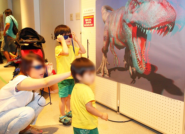 飛び出す3Ｄ恐竜展ポスターの飛び出しに驚く親子