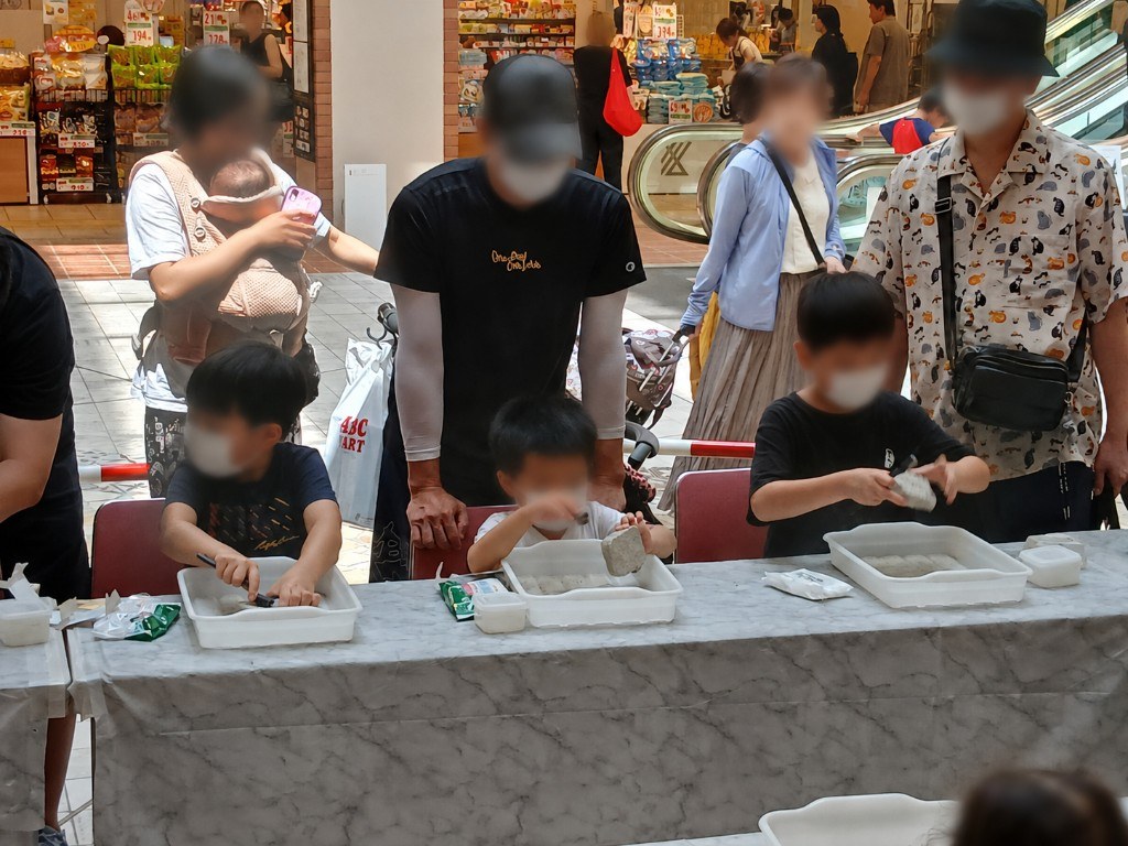 アンモナイト化石発掘体験の様子です。小学生のお子様を中心に、保護者の方も一緒に見守るファミリー層でにぎわいました。お顔は識別できないよう加工しています。