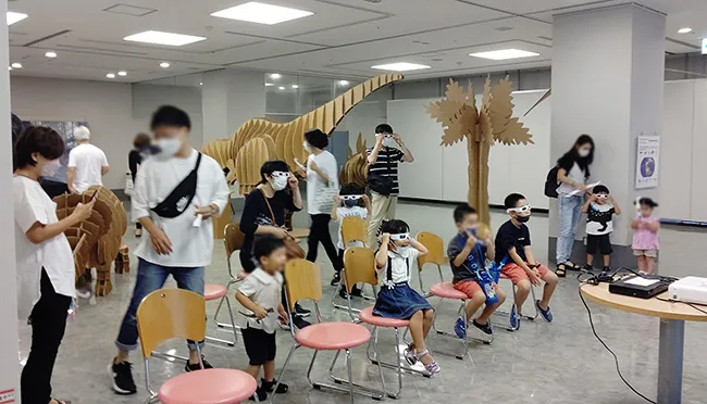 ３Dメガネをかけて、目の前に飛び出す恐竜を体験する子どもたち。