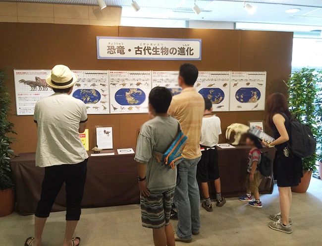 地球の歴史が学べる恐竜進化パネルに見入る大人たち。